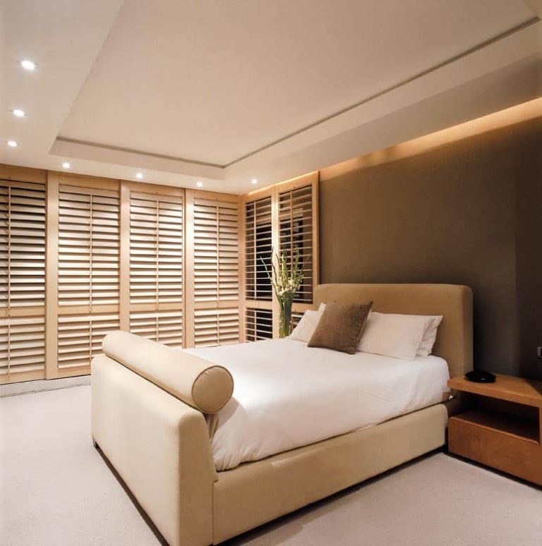 a bedroom with a bed dressed with Norman Full-height Shutters